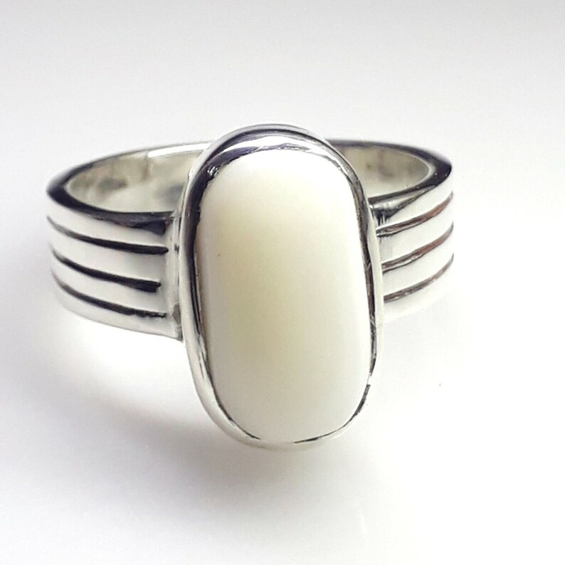 May include: A silver ring featuring a large, oval, off-white stone. The ring's band has three horizontal grooves on each side of the stone. The stone is set in a polished silver bezel.