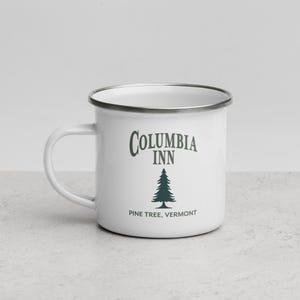 May include: White enamel mug with a silver rim and handle. The mug features the text "Columbia Inn" in a dark green script above a dark green pine tree graphic. Below the tree, the text reads "Pine Tree, Vermont."