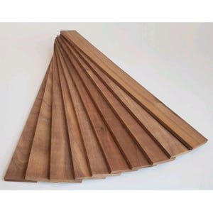May include: A fan of several unfinished, rectangular wooden planks. The planks are a warm brown color and appear to be made of hardwood. The planks are arranged in a semi-circular pattern, with the ends of the planks fanning out.