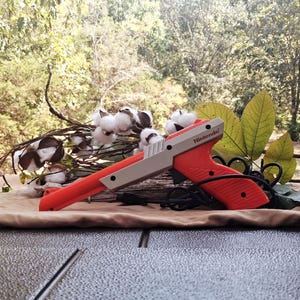 May include: A bright orange and light gray Nintendo Zapper light gun controller with a black trigger and cord. The device features the Nintendo logo printed on the side of the barrel and is positioned horizontally with a black handle grip.