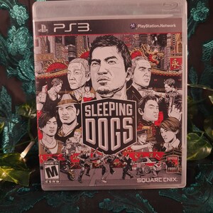May include: A PlayStation 3 video game case for Sleeping Dogs, featuring a graphic illustration of multiple characters against a city backdrop. The cover includes the PS3 logo, the ESRB Mature 17+ rating, and the Square Enix publisher logo.