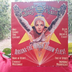 May include: A rectangular Ringling Bros. and Barnum & Bailey circus poster featuring a central illustration of a performer with arms raised. The red background includes a yellow star, text reading Airiana The Human Arrow Flies, and other slogans.