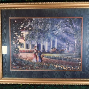 May include: Framed print of a Southern mansion with two figures walking on a path. The artwork features a horse-drawn carriage, lush trees, and a floral border, all within a gold-toned frame.