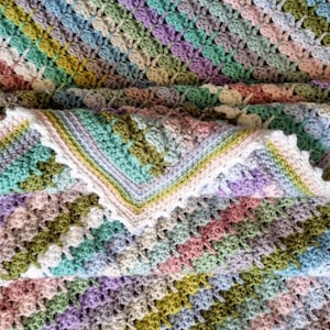 May include: A multi-colored crocheted blanket with a textured pattern. The blanket is made with a variety of pastel colors, including pink, blue, green, and purple.