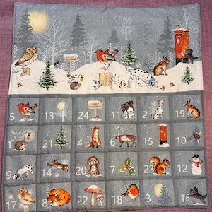 May include: A fabric advent calendar featuring a winter scene with a snowy landscape, pine trees, and a red postbox. The top section shows an owl, robin, and dalmatian. Below are twenty-four numbered pockets decorated with various animals, including foxes, rabbits, squirrels, and a snowman.