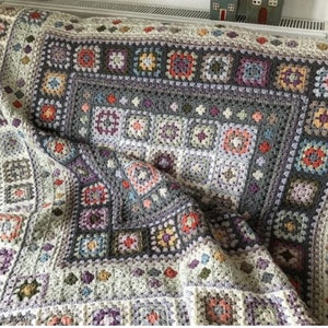 May include: A crocheted blanket with a multi-colored granny square pattern. The blanket is made with a variety of shades of gray, purple, pink, blue, and green yarn.