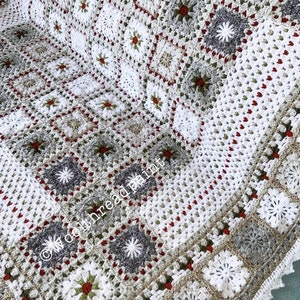 May include: A handmade, crocheted blanket with a geometric pattern in white, grey, and beige. The design incorporates square and star-shaped motifs with red and green accents. The blanket has a scalloped edge and the text "woolthreadpaint".