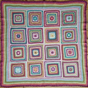 May include: A colorful crochet blanket with a square pattern. The blanket is made with different shades of pink, green, yellow, and brown yarn.