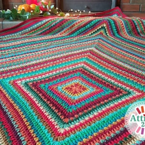 May include: A colorful crocheted throw blanket with a square pattern in the center. The blanket is made with a variety of colors, including red, green, blue, and yellow. The blanket is folded in half and is sitting on a wooden floor.
