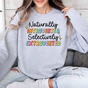 May include: A gray sweatshirt with the text "Naturally Introverted, Selectively Extroverted" in colorful letters.