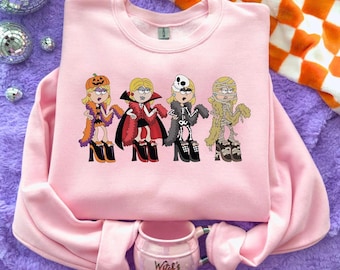 May include: A light pink crewneck sweatshirt featuring a graphic print of four cartoon characters dressed in Halloween costumes: a pumpkin, a vampire, a skeleton, and a mummy. Below the sweatshirt sits a small pink mug labeled Witch's Brew.