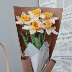 May include: A bouquet of crocheted daffodils in a brown paper wrapper with white tissue paper. The flowers are white with yellow centers.