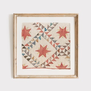 May include: A square framed textile wall art piece featuring a cream-coloured quilt fragment with red star motifs and intricate geometric patterns in shades of blue, brown, and red. The quilt displays detailed stitching and a vintage aesthetic.