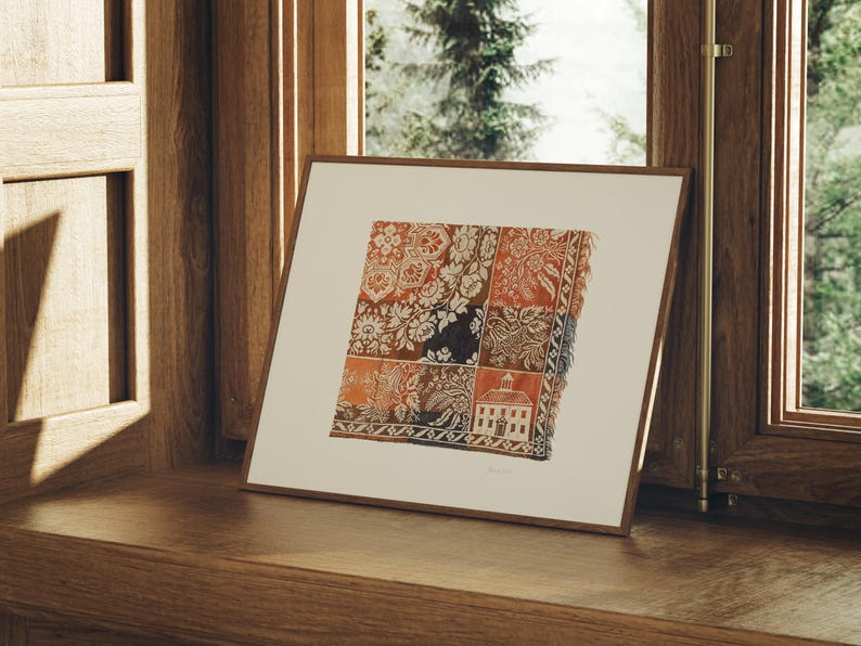 May include: A framed print featuring a detailed textile pattern with floral and geometric designs in shades of red, orange, and brown. The artwork is displayed on a wooden surface near a window, showcasing a classic aesthetic.