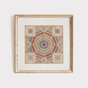 Puede incluir: Obra de arte enmarcada con un diseño de edredón geométrico y colorido. El edredón tiene un patrón central de estrella en tonos rojos, azules, verdes y crema, rodeado de bloques cuadrados más pequeños. El marco es de color dorado envejecido.
