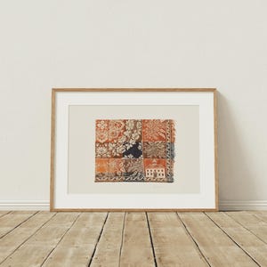 May include: Framed artwork featuring a patchwork design with floral and architectural patterns in shades of red, orange, and navy blue. The artwork is displayed in a natural wood frame, adding a touch of warmth to the piece. The artwork is displayed on a wooden floor.