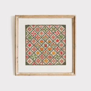 May include: Framed print of a quilt with a repeating pattern of red, green, and yellow floral and geometric designs. The quilt is set against a cream-coloured background and framed in a gold-coloured wooden frame.