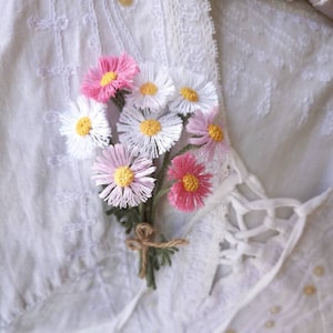 May include: A bouquet of white and pink crocheted daisies tied together with twine. The daisies are arranged in a cluster and have a delicate, handmade appearance.