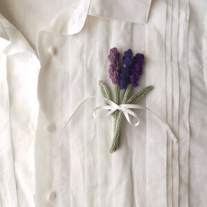 May include: A white button-down shirt with a crocheted lavender flower pin. The pin is tied with a white ribbon.