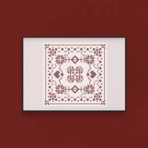 May include: Framed cross-stitch artwork featuring a symmetrical design in shades of brown on a cream background. The design includes floral and geometric patterns, hearts, and diamond shapes. The artwork is displayed in a black frame against a dark red wall.