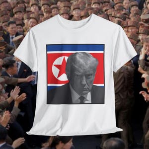May include: White t-shirt featuring a grayscale image of a man in a suit against a North Korean flag background. The image is centered on the shirt, with a crowd of people in the background.