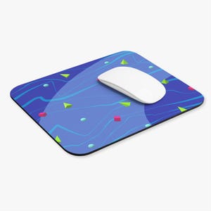 May include: A rectangular mousepad with a blue background and a pattern of wavy lines, geometric shapes, and dots. A white wireless mouse rests on the mousepad. The shapes are in shades of green, pink, and blue.