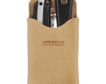 May include: A tan leather tool pouch with the text "AMERICAN TRADESMAN" embossed on the front. The pouch contains a utility knife, a black folding knife, and a silver blade. The pouch is open at the top, revealing the tools inside.