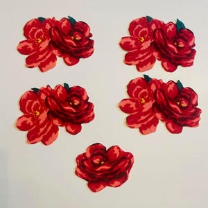 May include: Five fabric patches shaped like red roses. Four of the patches feature a cluster of two flowers with dark green leaves, while the fifth patch at the bottom is a single red rose. Each patch displays shades of deep red and light pink.