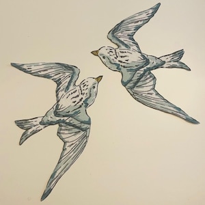 Puede incluir: Dos pájaros dibujados a mano en vuelo, representados en blanco, gris y azul. Los pájaros tienen patrones de alas detallados y picos amarillos, sobre un fondo crema. La obra de arte evoca una sensación de libertad y naturaleza.