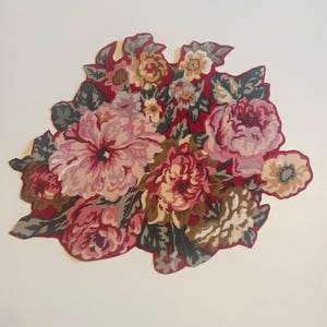 May include: A floral design featuring a cluster of stylized flowers in shades of pink, red, and cream. The arrangement includes various flower types with green and brown leaves, set against a red background.