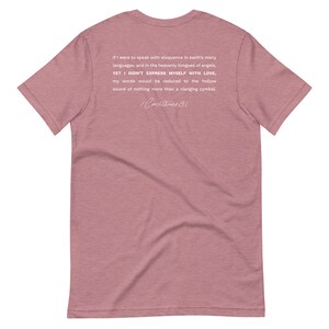 May include: A dusty rose t-shirt with white text on the back. The text reads, "If I were to speak with eloquence in earth's many languages...YET I DIDN'T EXPRESS MYSELF WITH LOVE...1 Corinthians 13:1."