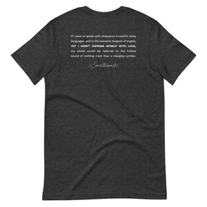 May include: Dark gray t-shirt with white text from 1 Corinthians 13:1. The text reads, "If I were to speak with eloquence in earth's many languages...YET I DIDN'T EXPRESS MYSELF WITH LOVE..." A stylish, comfortable tee.