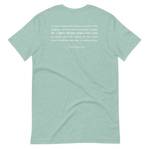 May include: A light green t-shirt with white text. The text includes a quote from 1 Corinthians 13:1, discussing the importance of love. The shirt is a short-sleeved crew neck.