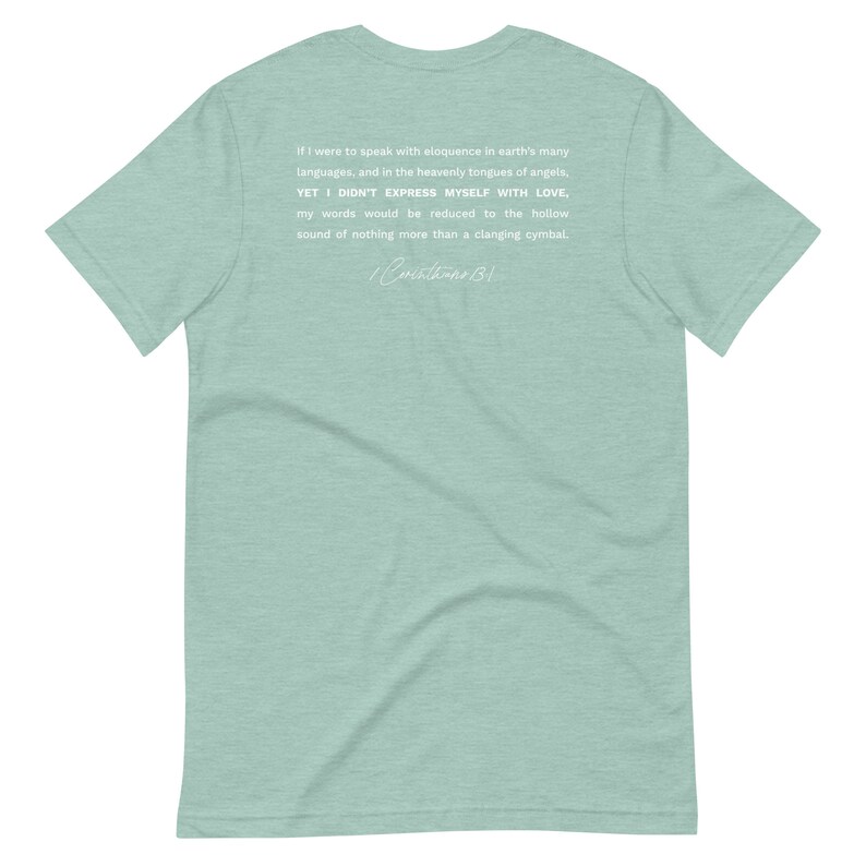 May include: A light green t-shirt with white text. The text includes a quote from 1 Corinthians 13:1, discussing the importance of love. The shirt is a short-sleeved crew neck.