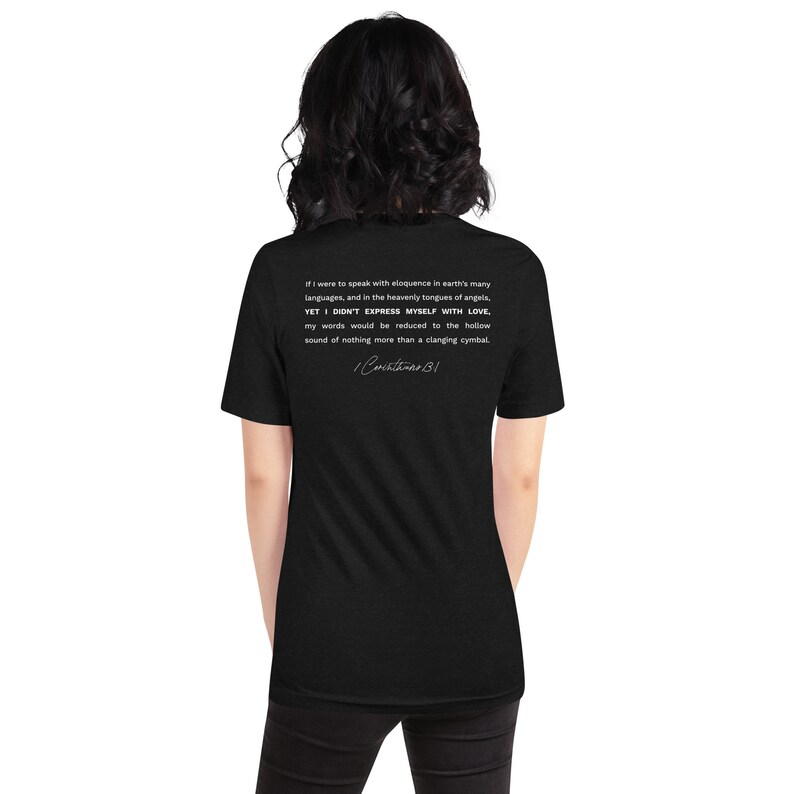 May include: Black t-shirt with white text on the back. The text includes a quote from 1 Corinthians 13:1 about the importance of love. The shirt is a short-sleeved, unisex style.