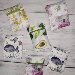 Könnte beinhalten: Sechs kleine Reißverschlusstaschen mit verschiedenen Designs. Die Taschen sind weiß mit verschiedenen Aquarell-Illustrationen. Die Designs beinhalten einen Koala, eine Avocado, einen Wal, einen Oktopus und Blumenmuster.