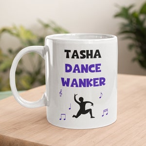 May include: White ceramic mug with a black silhouette of a dancer and the text "Tasha Dance Wanker" in purple. Musical notes are printed around the dancer.