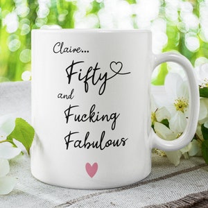May include: White ceramic mug with black text that reads "Claire... Fifty and Fucking Fabulous" with a pink heart above the word "Fifty" and a pink heart below the word "Fabulous".