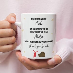 May include: White ceramic mug with the text "BEHIND EVERY Cub WHO BELIEVES IN THEMSELVES IS A Akela WHO BELIEVED IN THEM FIRST! Thank you Sarah". The mug has a red tie and brown boot graphic.