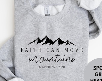 May include: Sport grey heather sweatshirt with the text "FAITH CAN MOVE mountains" and "MATTHEW 17:20" in black. A black mountain range graphic is above the text. The sweatshirt is a crew neck style.