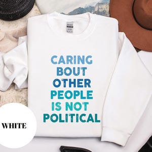 Bold statement sweatshirt with the phrase Caring About Other People Is Not Political, promoting kindness, activism, and human rights.