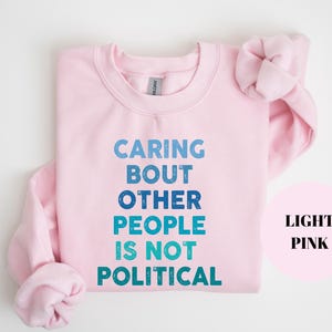 Bold statement sweatshirt with the phrase Caring About Other People Is Not Political, promoting kindness, activism, and human rights.