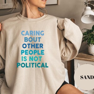 Bold statement sweatshirt with the phrase Caring About Other People Is Not Political, promoting kindness, activism, and human rights.