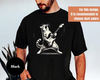 May include: Black t-shirt featuring a black and white illustration of a cat playing an electric guitar. The cat is depicted with its mouth open, as if singing. The text on the image says, "For this design, it is recommended to choose dark colors."