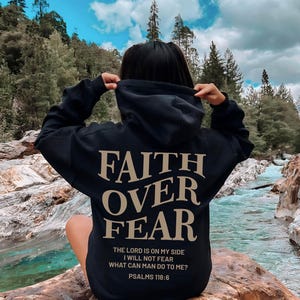May include: Black hoodie with the text "FAITH OVER FEAR" in gold lettering. The text "THE LORD IS ON MY SIDE I WILL NOT FEAR WHAT CAN MAN DO TO ME? PSALMS 118:6" is printed in smaller gold lettering below the main text.