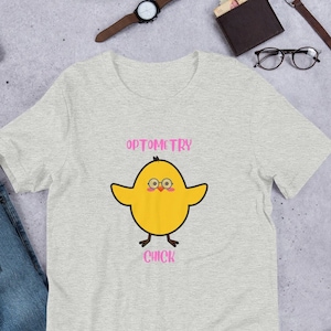 Puede incluir: Una camiseta gris jaspeada con un pollito amarillo que lleva gafas y el texto "OPTOMETRY CHICK" en rosa.