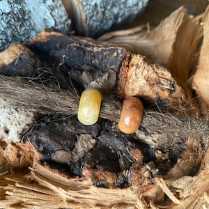May include: Two round, natural stone beads in yellow and brown colors. The beads are strung on a brown dreadlock.