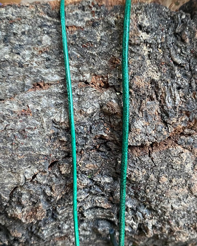 Puede incluir: Dos hebras de cord&oacute;n o cuerda verde sobre un fondo rugoso, marr&oacute;n y texturizado.