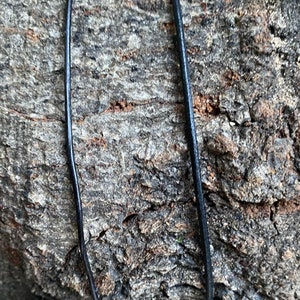 Puede incluir: Primer plano de un cord&oacute;n de cuero negro sobre un fondo de madera rugoso y texturizado.