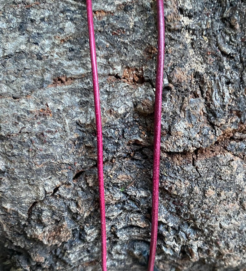Puede incluir: Dos cordones largos, delgados y de color burdeos se muestran sobre un fondo rugoso, gris y texturizado.